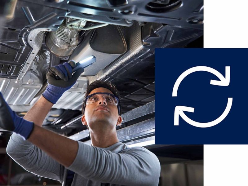 Un collaboratore Service VW sta esaminando la sottoscocca di un veicolo Volkswagen, accanto c’è il simbolo del riciclo.