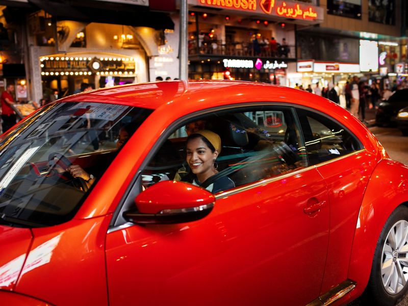 Die Lichter der Straßenlaternen und Geschäfte spiegeln sich im roten Lack des Beetle wider – Ausflug mit VW Auto