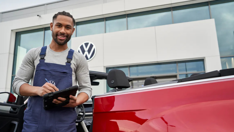 Volkswagen monteur met tablet in zijn handen lacht naar de camera, staat buiten bij een dealer naast een t-roc cabrio