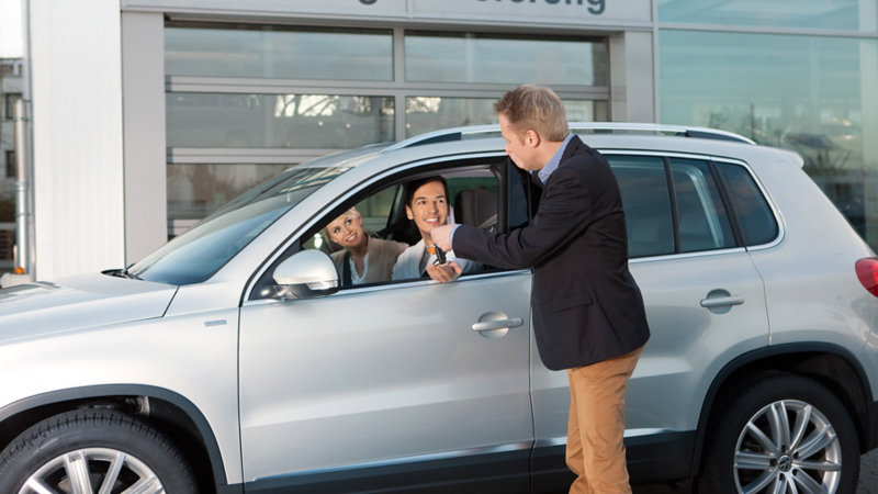 A man and woman sitting in a car while a service manager in a suit stands beside them