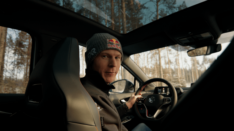 Johan Kristofersson sitter i förarsätet på en Volkswagen. Bilden tagen från baksätet i bilen