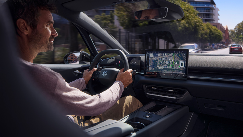 Person sitzt am Steuer eines VW ID.3 Neo, Navigationskarte auf Zentraldisplay, Stadtstraße mit weiteren Fahrzeugen sichtbar.