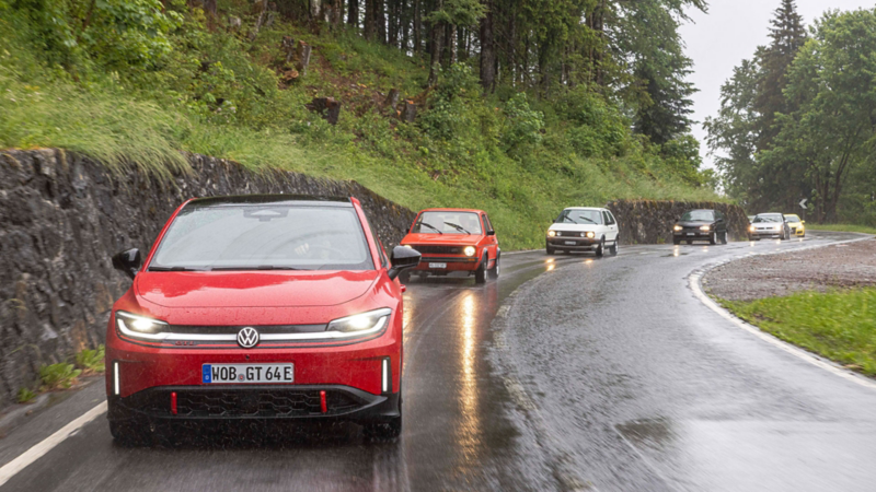 Diverse generazioni della Volkswagen GTI su una strada di montagna sotto la pioggia.