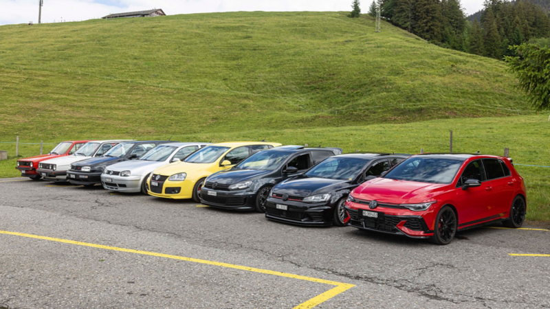 Überblick aller Generationen des Volkswagen GTI nebeneinander auf einem Parkplatz in den Alpen.