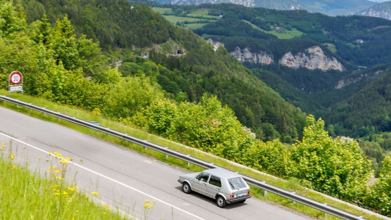 Une vieille VW Golf roule sur une route de campagne