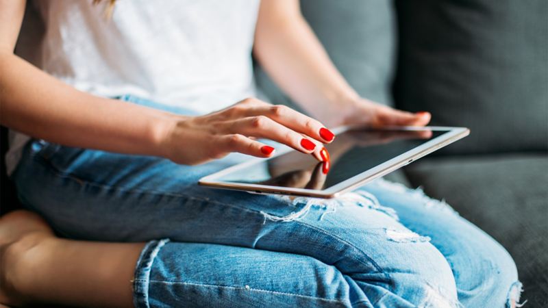 Eine Frau sitzt mit einem Tablet auf der Couch