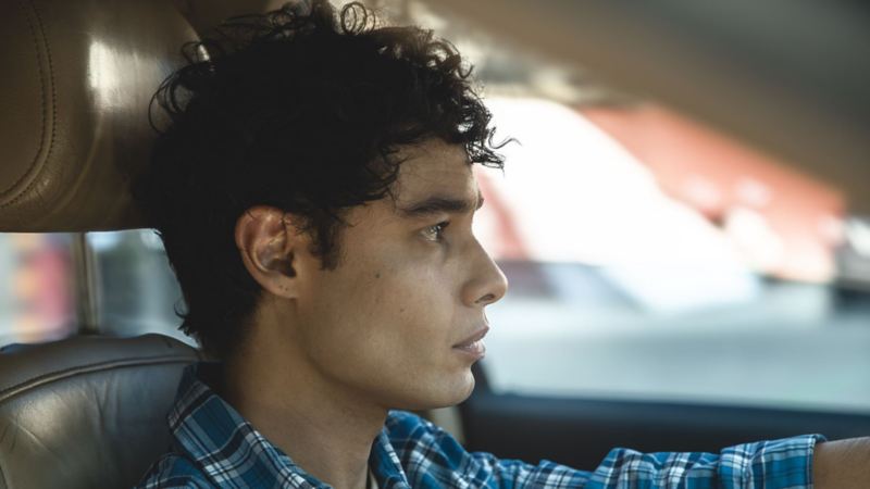 Hombre de cabello crespo y camisa de cuadros maneja un auto Volkswagen. 