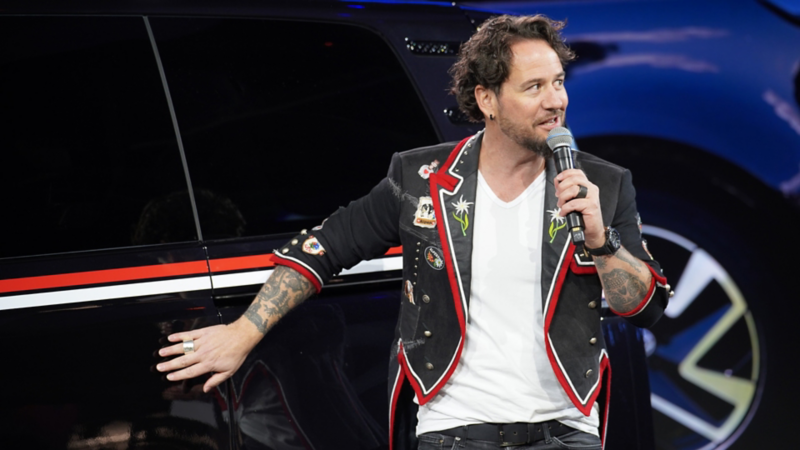 Marc Trauffer parla al microfono sul palco accanto a un VW Bulli personalizzato.