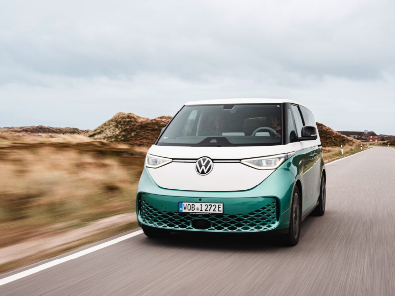 En grön-vit VW ID. Buzz kör på en kustväg.