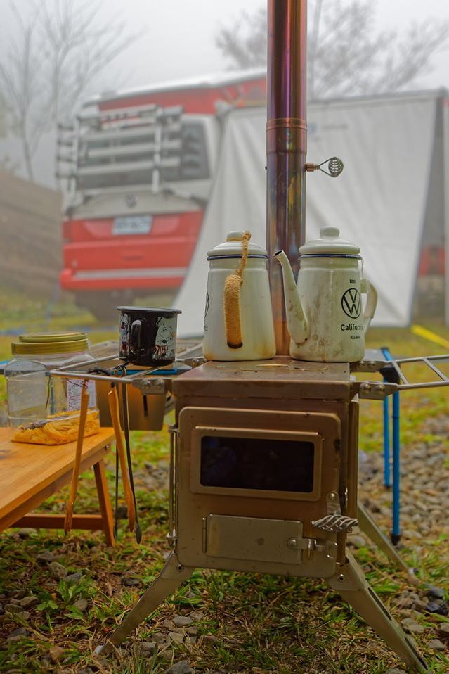 車主露營器具照，印有福斯商旅logo的琺瑯水煮壺放在置物桌上，背景是紅白雙色California停在遠方