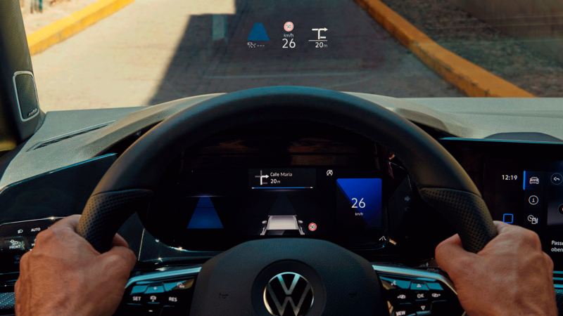 Detalle de la pantalla de visualización frontal vista a través de un volante cogido por dos manos
