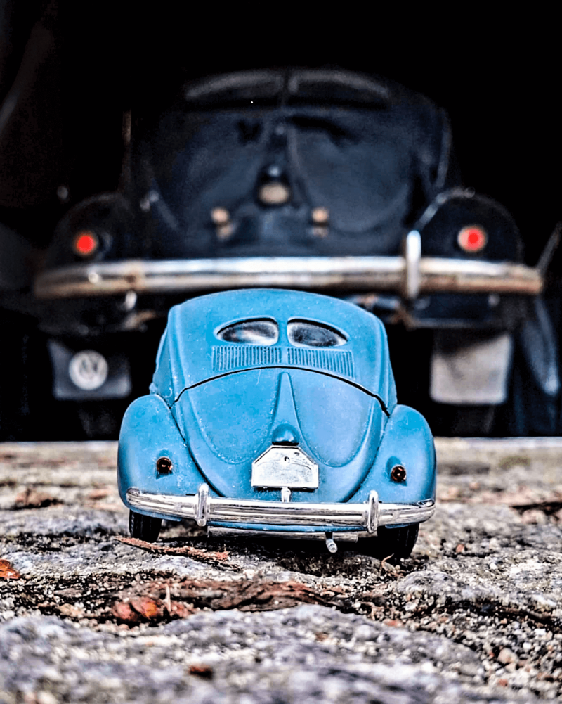 Niebieski, miniaturowy Volkswagen Beetle, a za nim pełnowymiarowa wersja. 