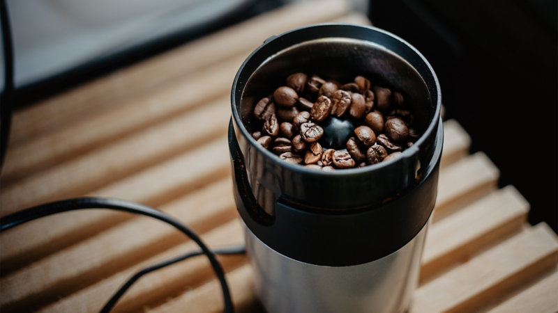 Close-Up auf eine elektrische Kaffee-Mühle gefüllt mit Kaffeebohnen.