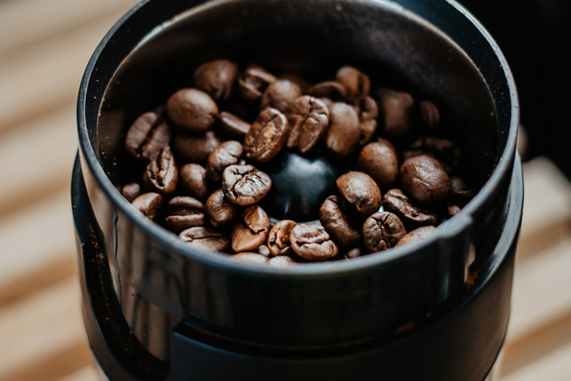 Close-Up auf eine elektrische Kaffee-Mühle gefüllt mit Kaffeebohnen.