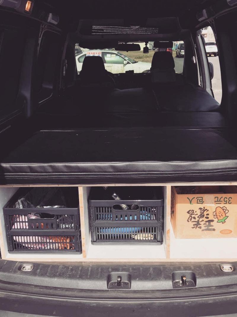 改裝的Caddy Van後廂空間，做出隔層的木板上攤平放置黑色皮墊，木板下方除了隔層、也用黑色收納籃及紙箱收納各式雜物