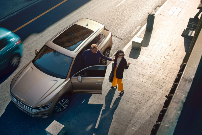 Widok z lotu ptaka. Volkswagen jest zaparkowany przy ulicy. Wychodzi z niego mężczyzna i łapie kobietę stojącą na chodniku.