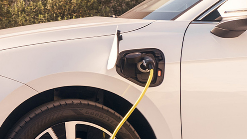 Biały VW Passat plug-in hybrid ładuje się przy stacji ładowania