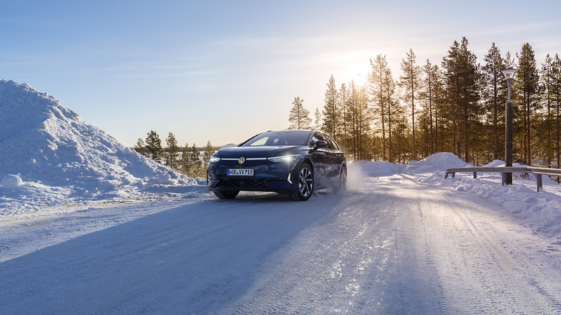Ein blauer ID.7 fährt auf einer verschneiten Straße mit schneeweißer Landschaft und Bäumen im Hintergrund.