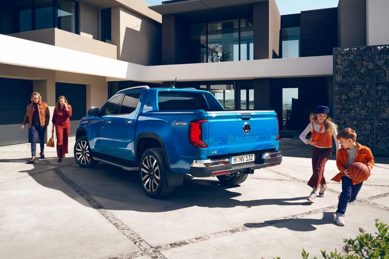 Der VW Amarok parkt in einer Auffahrt und zwei Frauen gehen an ihm vorbei und ein Junge und ein Mädchen spielen hinter dem VW Amarok.