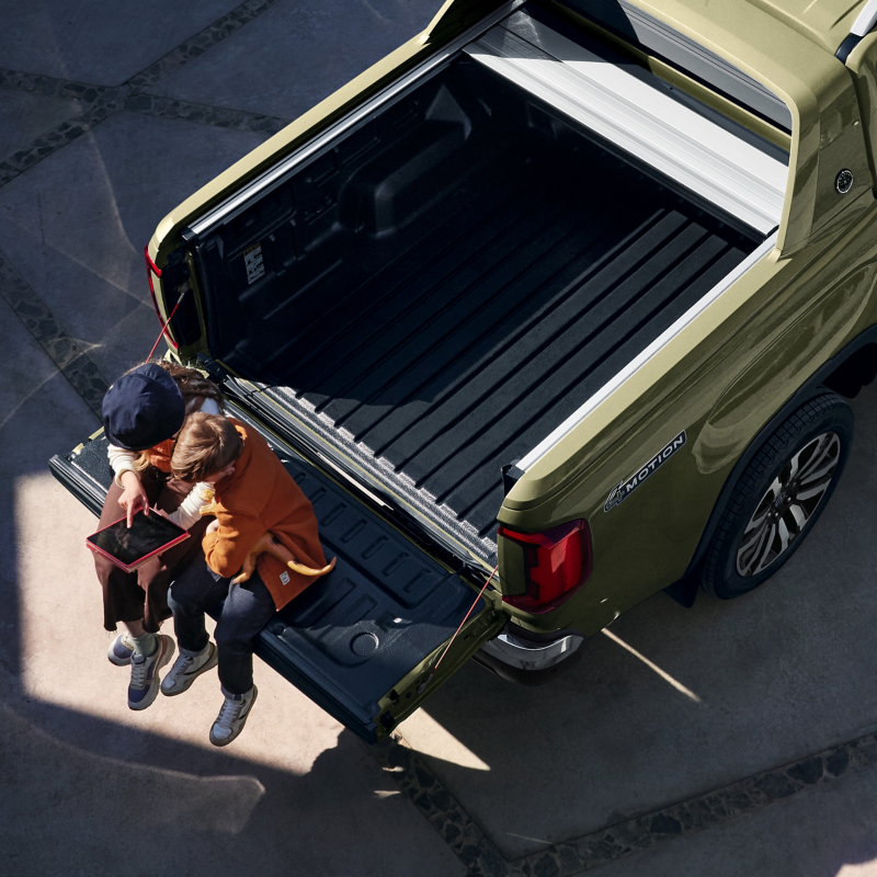 Zwei Kinder sitzen auf der Ladefläche eines Amarok und blicken auf ein Tablet.