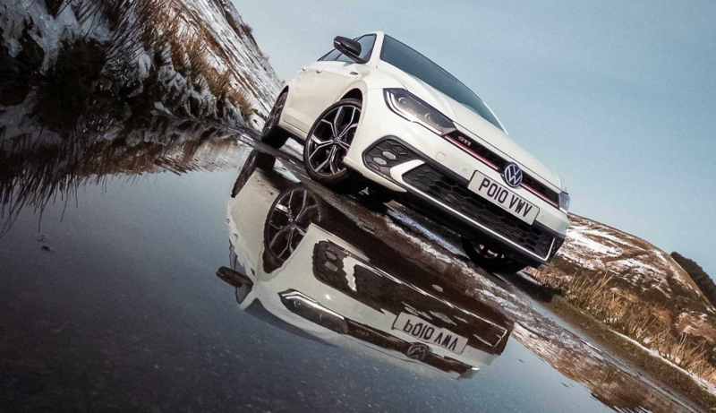 A low front angle of a white Polo GTI parked on a mountain road reflected in a puddle