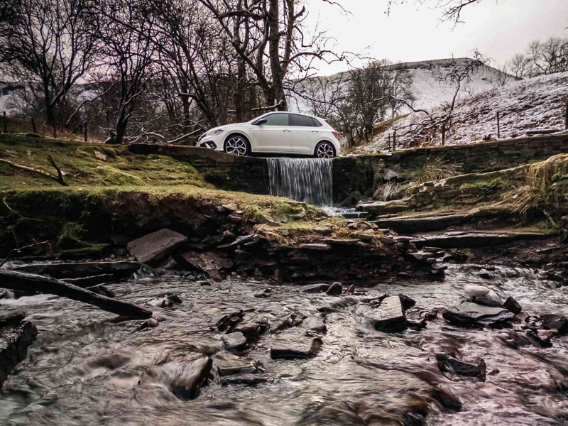 A white Polo GTI driving over a small waterfall leading into a rocky creak