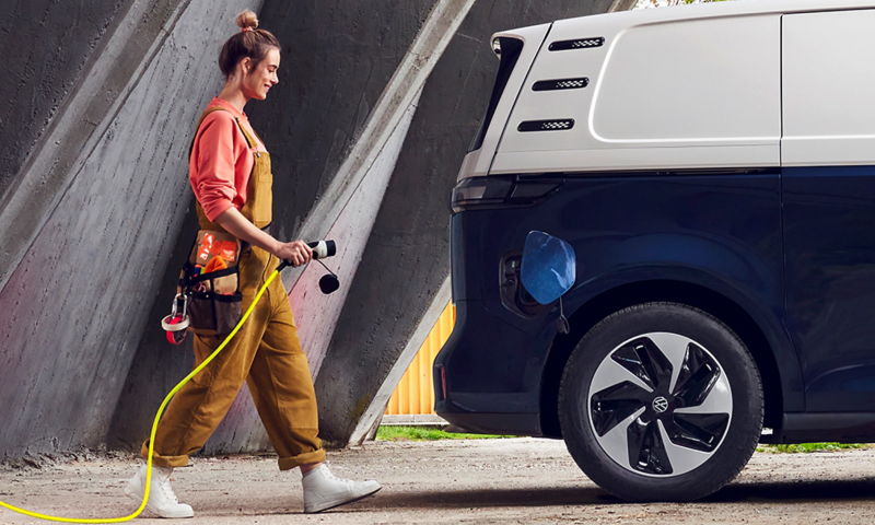 A tradeswoman walks towards an ID. Buzz Cargo with a charging cable in her hand.