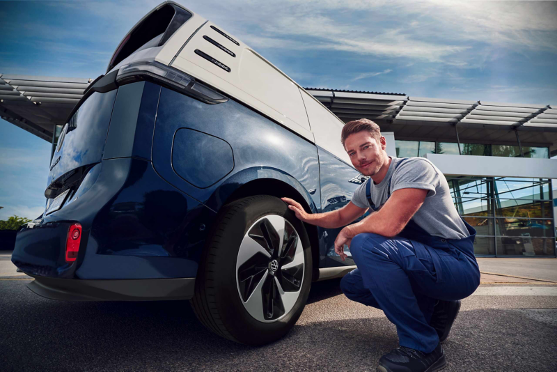 Un mécanicien se tient à côté d’un Volkswagen Multivan eHybrid surélevé orange.