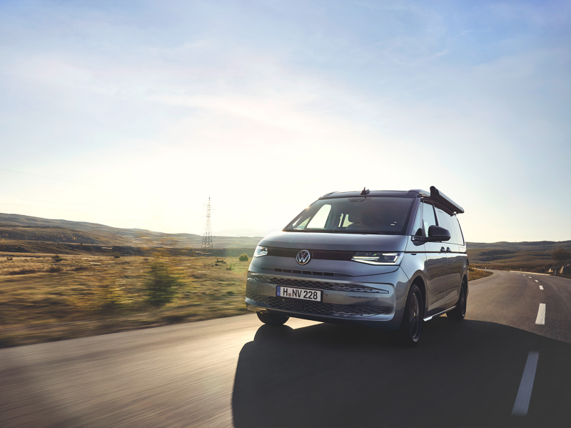 Ein VW Multivan fährt auf einer Landstraße, im Hintergrund scheint die Sonne