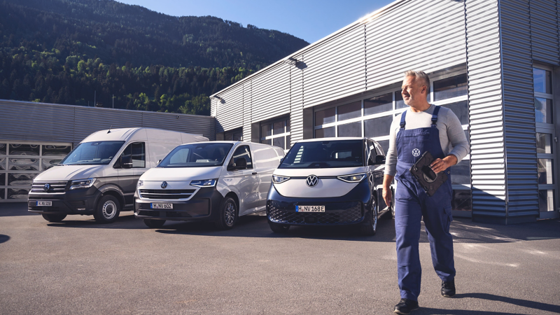 Ein VW Servicemitarbeiter und eine Flotte VW Nutzfahrzeuge vor einer Werkstatt.