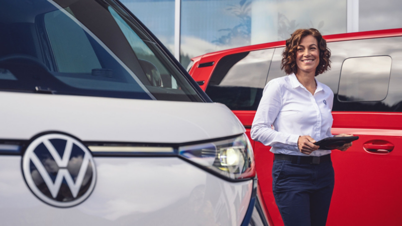 Volkswagen Mitarbeiterin mit Tablet zwischen zwei Nutzfahrzeugen. 
