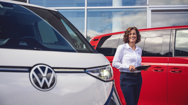Eine Servicepartnerin von VW mit Tablet in der Hand steht vor VW ID. Buzz Modellen.