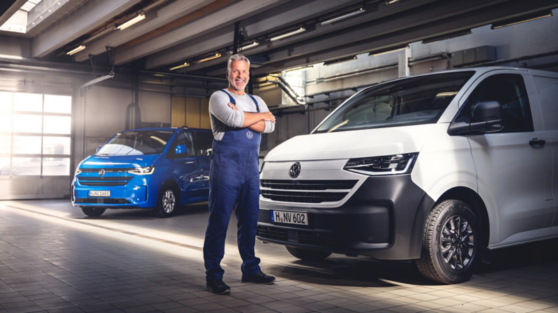 Mitarbeiter steht in einer Servicecenter-Werkstatt vor VW Fahrzeugen.