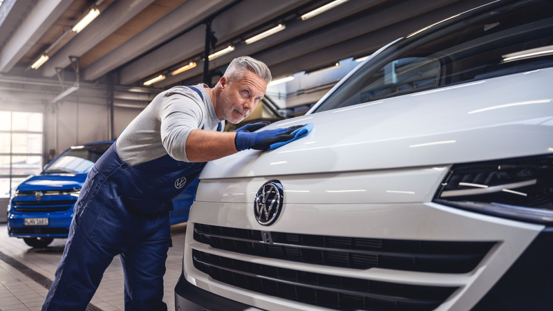 Ein Mechaniker steht an einem Volkswagen Transporter und streicht über die Motorhaube.