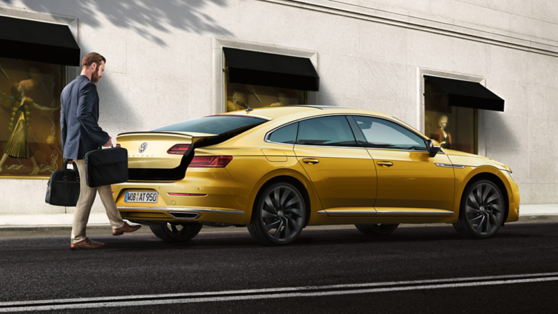 Un uomo apre il bagagliaio di Volkswagen Arteon versione 'R-Line' tramite il sistema 'Easy Open', con sensori di movimento del piede.