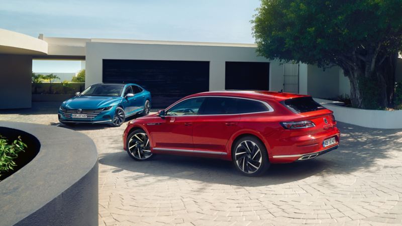 Ein blauer VW Arteon und ein roter Arteon Shooting Brake stehen vor einem modernen Haus
