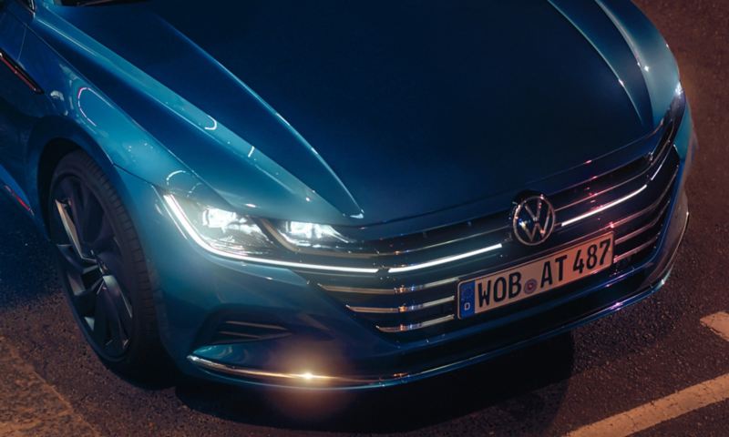 .Vue détaillée de l'avant d'une Volkswagen Arteon Elegance bleue avec les phares allumés.