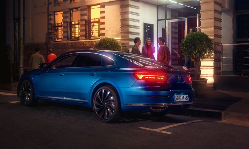 Niebieski Volkswagen Arteon zaparkowany przed luksusowym budynkiem w mieście, widok na tył nadwozia i tylne światła LED 3D.