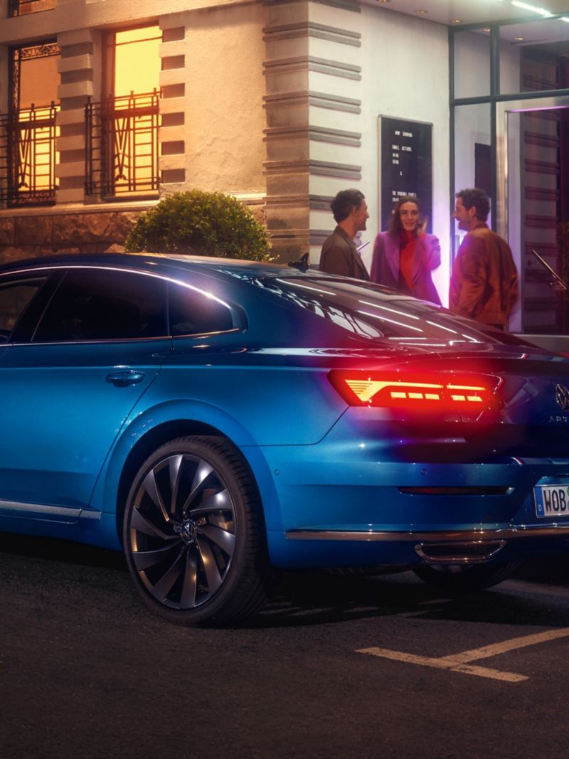 Niebieski Volkswagen Arteon zaparkowany przed luksusowym budynkiem w mieście, widok na tył nadwozia i tylne światła LED 3D.