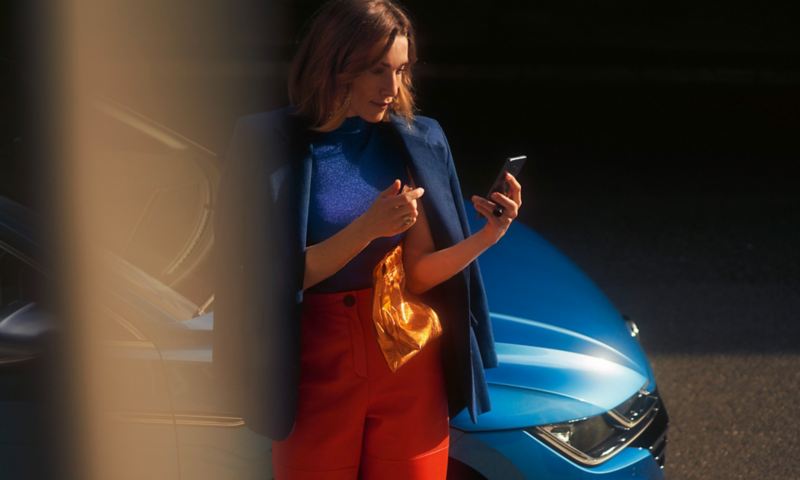 En kvinde læner sig op ad en VW Arteon og benytter Wi-Fi-hotspottet, som er integreret i ”Streaming & Internet” (ekstraudstyr), med sin mobiltelefon.