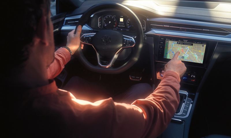 Ein Mann fährt im VW Arteon Shooting Brake mit Multifunktionslenkrad und bedient das große Farbdisplay mit Navigationsansicht.