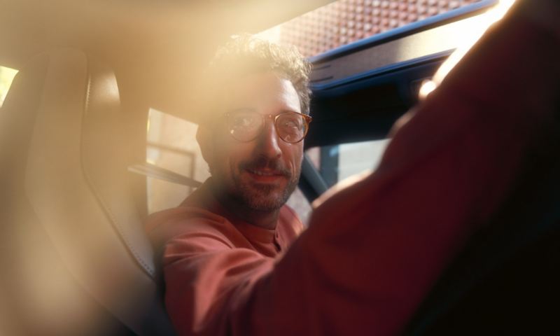Mann sitzt auf Fahrersitz und guckt nach hinten durch die Heckscheibe, Sonnenschein fällt durch das geöffnete optionale Schiebedach.
