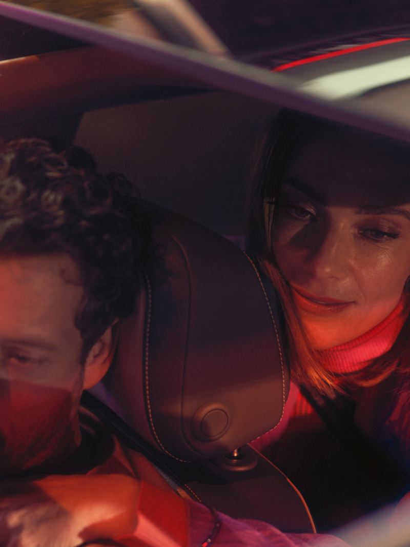 Blick durch das geöffnete optionale Panoramadach eines VW Arteon auf Mann und Frau, die auf Beifahrer- und Rücksitz sitzen.