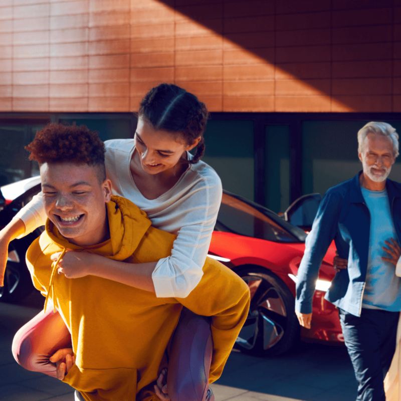Photo d'une famille heureuse avec un véhicule électrique VW en arrière-plan, lien vers la page « Famille ID. »