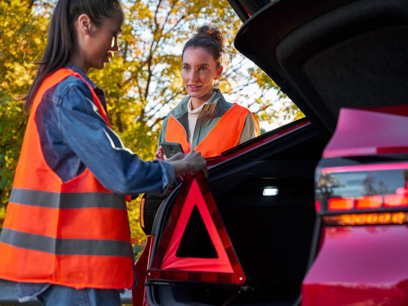 Two women with safety vests and warning triangle next to VW ID.5 GTX