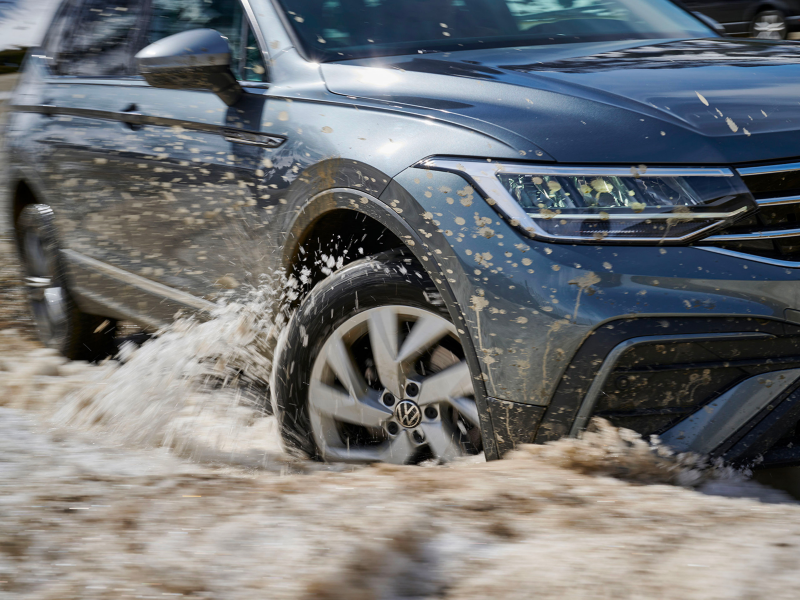 VW car drives through mud and water, with the left front wheel in focus