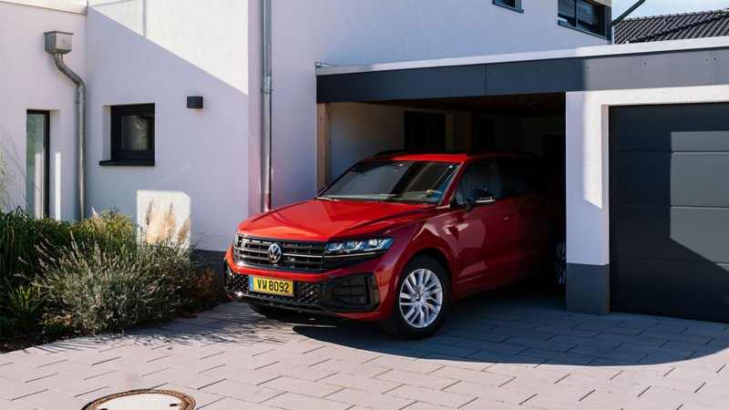 Un Touareg R-Line rouge est garé dans le garage d'une maison individuelle blanche.