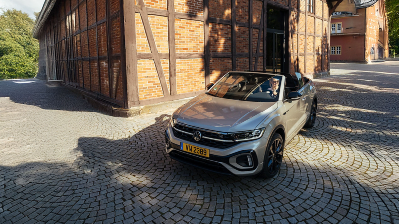 T-Roc Cabriolet stationné devant une maison à colombages avec une femme au volant portant des lunettes de soleil.