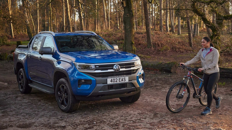 A VW Amarok parked in a woodland area with a woman holding a bike standing next to it.
