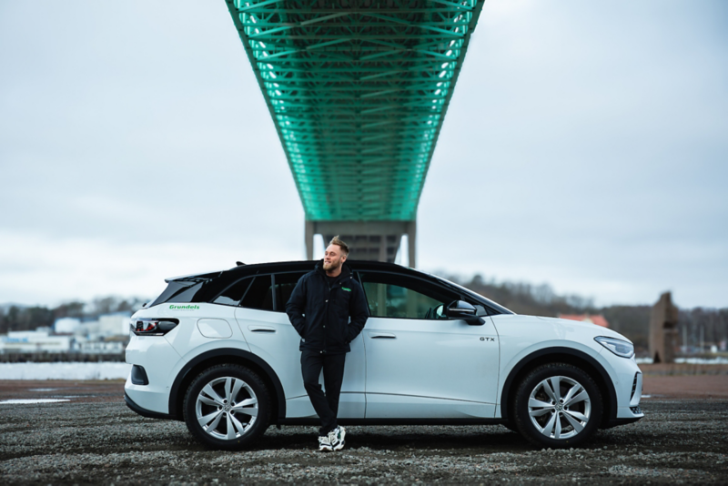 Anton Thölén står under en bro och lutar sig mot en vit Volkswagen ID.4.